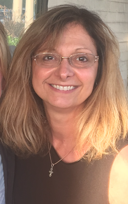 A woman with blonde hair and glasses smiles at the camera