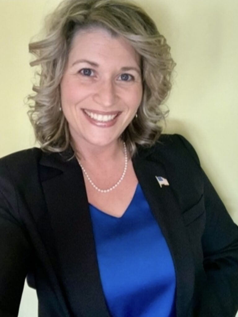 A blond woman in a business suit smiles at the camera