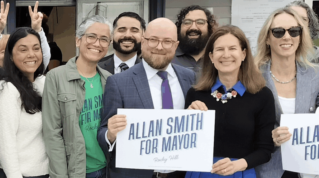 A smiling group of people behind the sign, Allan Smith for Mayor